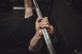 A pair of hands grip a barbell, pushing upward.