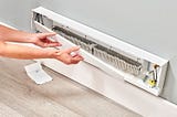 white baseboard heater cover being placed back