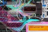 Stylised photograph of an eletronics prototyping breadboard with wires, chips and a display that says ‘Zolatron 64’. For decorative purposes only.