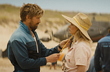 A blonde man in a blue jumpsuit holds the strings on a hat worn by a blonde woman. Fall Guy movie review, action, comedy