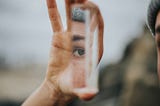 Hand holding a piece of glass reflecting an eye and eyebrow.