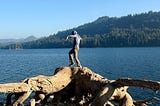 Author dances on a giant stump at the edge of a lake.