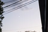 Picture showing an indigo gradient sky along with electric cables coming from the top of a house to the right, to a tree to the left, with a waxing crescent moon visible in the middle.