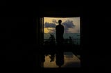 person standing in darkened room peering out the window at a cloudy sky, dark and ominous