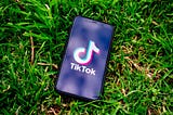 An iphone lying in the grass opened to TikTok