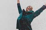 A Black woman in green, jumps for joy, tossing glitter in the air