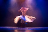 Dancer spinning on stage, blurred under purple stage lights, symbolizing the process of transformation and expansion