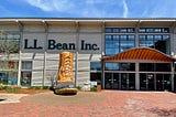 A photograph showing a huge shopfront with L.L. Bean Inc. written in large letters on the front of the store. The shopfront is mostly glass with a large entrance way. There is a giant boot on the brick walkway leading up to the store.