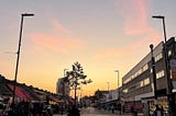A picture of a market road in London in the evening with few people walking around, with a beautiful summer sunset in the background