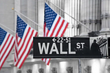 The Wall Street street sign with American flags in the background.