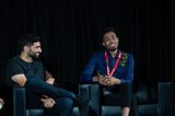 Nima Ghamsari, a Persian man in a black t-shirt, and Ulyssses Smith, a Black man in a blue collared shirt, on stage