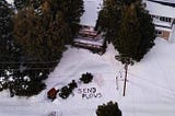 Aerial view of a message written in the snow in Crestline California that reads: “Send Plows”
