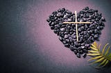 A matchstick cross on a stone heart, with a palm branch next to it