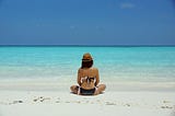 Women sitting cross-legged on beach staring out at the ocean.