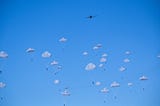 Parachutists drop from a distant plane against clear blue sky.