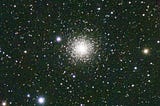 Globular cluster M15, a dense cluster of stars at the center the star field shining brightly. There are a number of bright objects surrounding it.