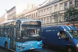 A blue bus and a blue van side by side on a street. The bus is a Budapest city bus.