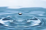 A single water droplet suspended over a body of water. Article about dehydration by Harlow Journey.