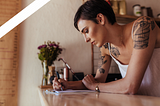 woman with arm tattoos writing at desk