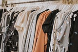 A clothing rack with shirts hung from hangers. Most grey and some orange.