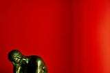bronze statue in thinking pose with a red background