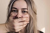 A sad, abused woman has a hand placed over her mouth to silence her.