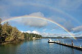 A double rainbow arches across a ship at a dock