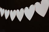 A string of white paper hearts stands out against a black background.