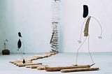 Sculpture by artist Anne Cécíle de Bretagne, small driftwood figurines walking towards an endless ladder on the other side of the room.