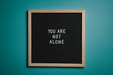 A word board with the phrase ‘You Are Not Alone’ written on it