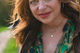 A GenX white woman named Karen Fleshman wearing a green shirt, in front of a green lawn, with sunshine in her hair.