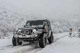 A black Jeep driving through a snowstorm with its headlights on