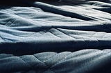 A wrinkled blue bed sheet with vividly contrasted shadows between each wrinkle.