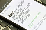 A photo of a phone resting on a laptop keyboard. The phone is open to a browser page, “bard.google.com”, and the page header reads “Bard can explain why large language models might make mistakes” before showing a confirmation that the user has been added to a waitlist.