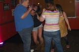 Picture of a man singing while ladies dance around him.