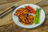 Pork chops plated with tomatoes and asparagus.