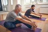 Two men on their own yoga mats, stretching.