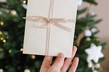 Woman’s hand holding white Christmas card against evergreen background