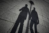 Silhouette of two men holding hands on the sidewalk.