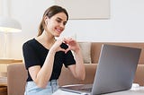 Woman in front of computer making heart shape with hands.