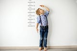 A child measuring his height against a large ruler on a wall