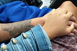 Mixed couple holding hands, man has a tatoo on his forearm.