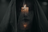 A lit candle shines through a woman’s sheer veil, casting light on her face.