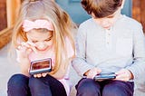 Photograph of two children playing on mobile devices