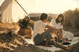 A man and woman on the beach with a picnic and a sun umbrella for shade