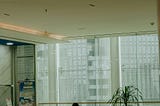 Person sitting alone in a large empty lobby, head down, surrounded by space