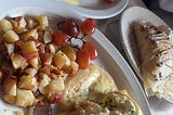 A vertical photo of many food items from the Uptown establishment Crepes and Grapes. This includes an omelet, potatoes, a crepe, and grapes!