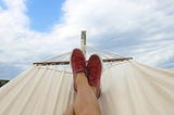 man-relaxing-in-hammock-with-red-sneakers-blue-cloudy-skies