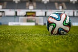 A soccer ball on a field with stands behind