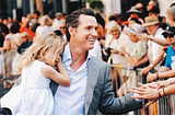 Governor Gavin Newsom of California greets voters while carrying his daughter in the times before COVID.